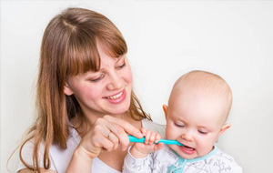 Young mother brushing baby’s teeth